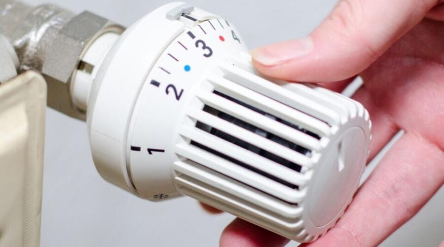 Eine Hand stellt die Temperatur an einem weißen Heizkörperthermostat ein, indem sie den Regler von Stufe 2 auf Stufe 3 dreht.