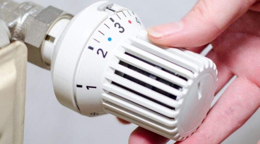 Eine Hand stellt die Temperatur an einem weißen Heizkörperthermostat ein, indem sie den Regler von Stufe 2 auf Stufe 3 dreht.
