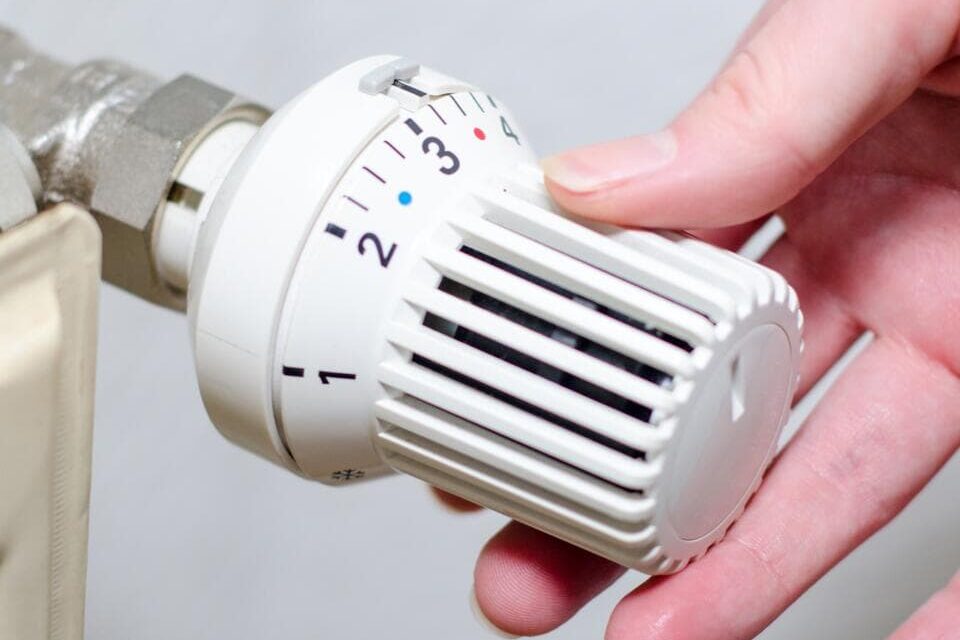 Eine Hand stellt die Temperatur an einem weißen Heizkörperthermostat ein, indem sie den Regler von Stufe 2 auf Stufe 3 dreht.
